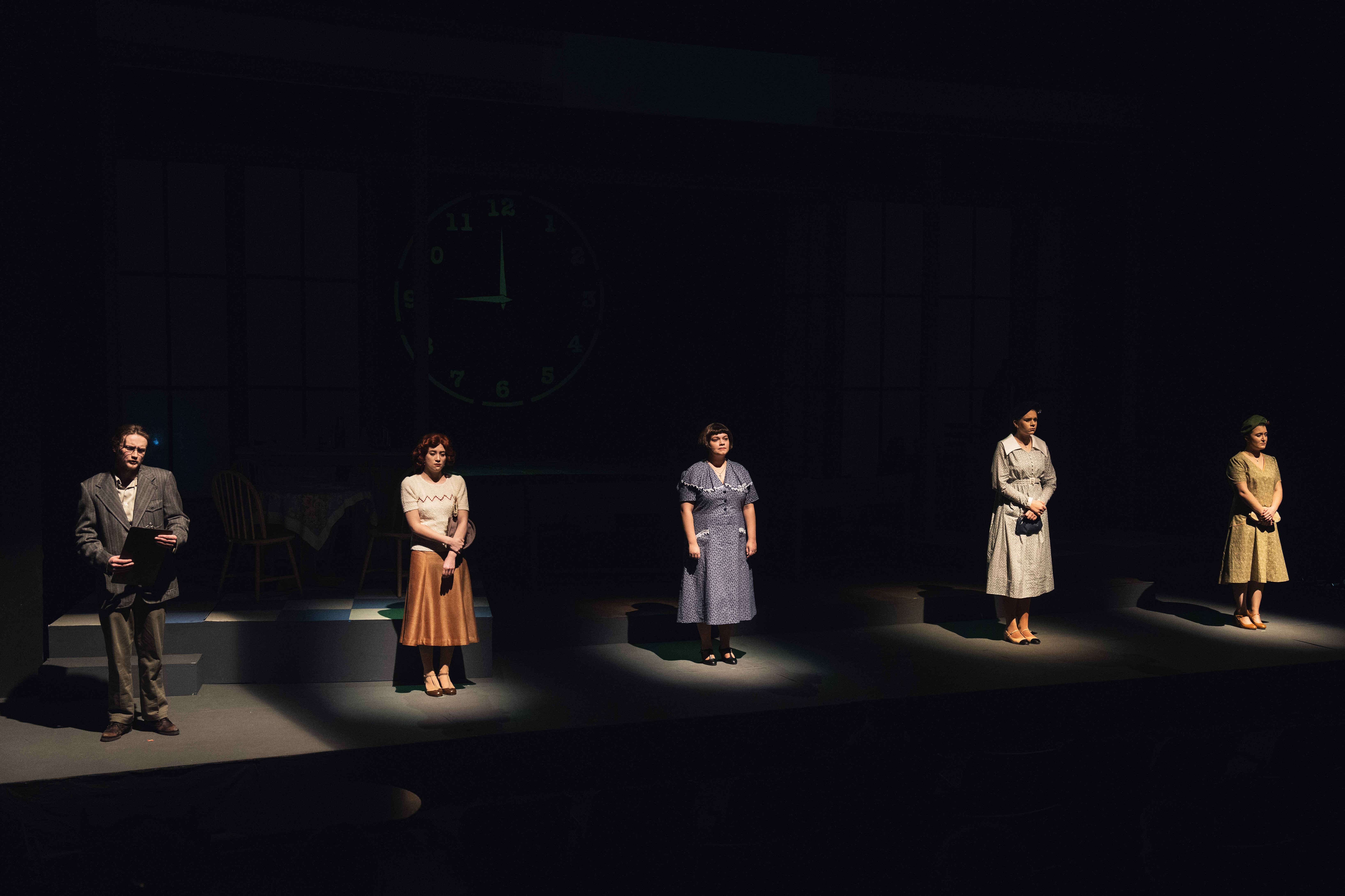 four women and a man stand in spotlights across a stage