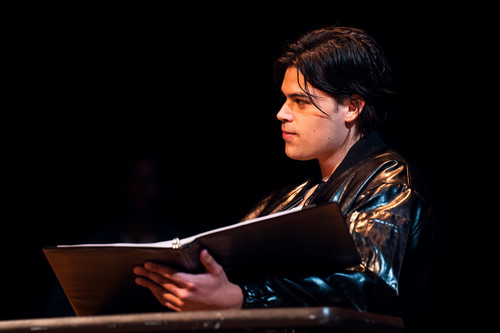 A seated Latino man in a leather jacket leads on a table