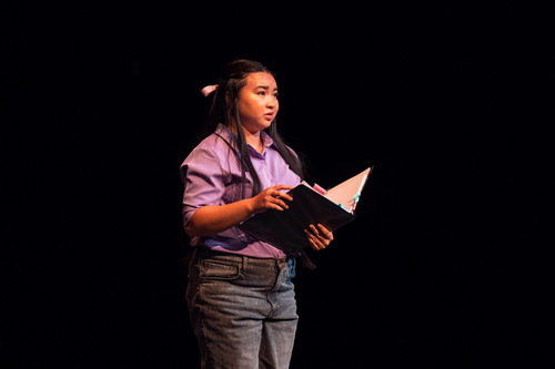 A woman in a purple shirt reads from a script