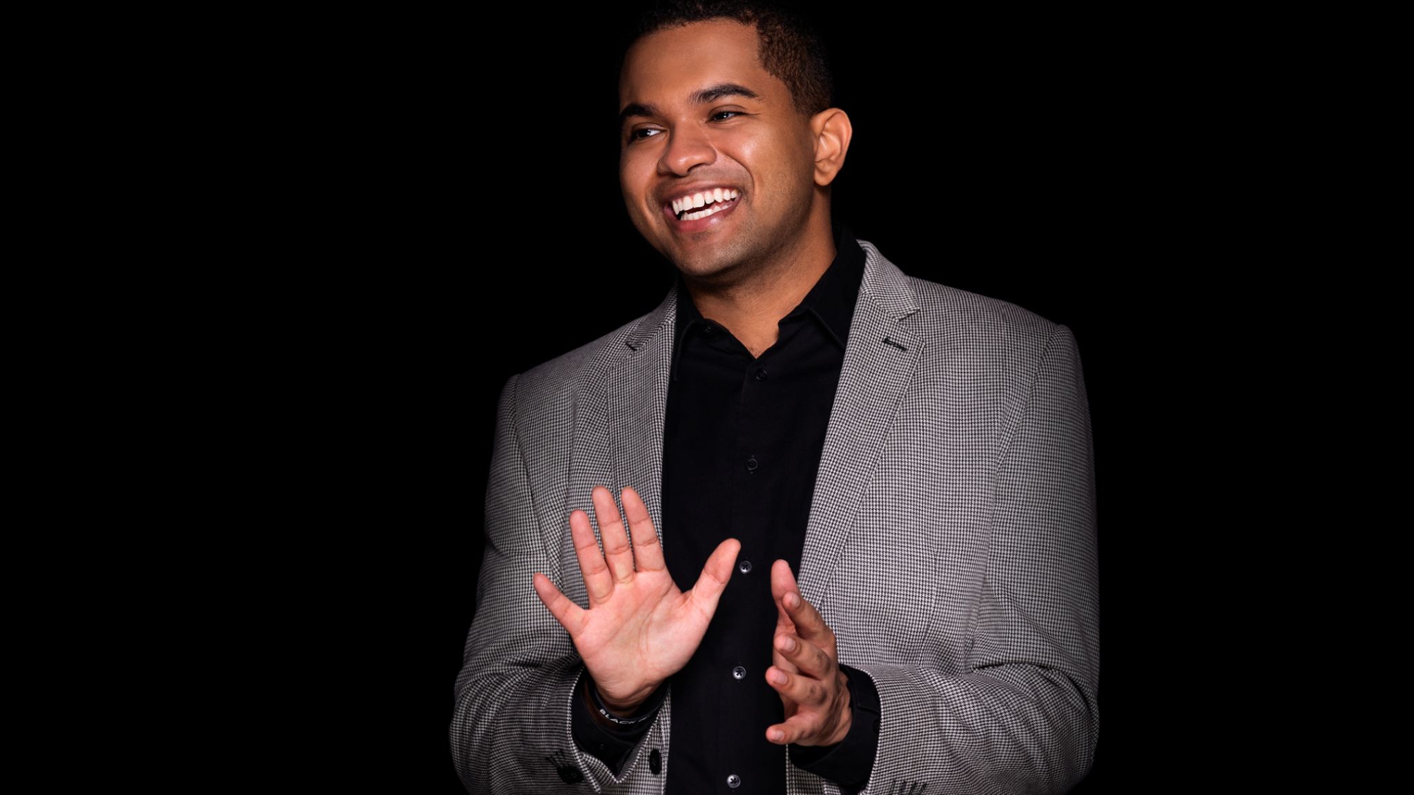 Taylor Stewart, a black man smiling in a gray suit in a dark room
