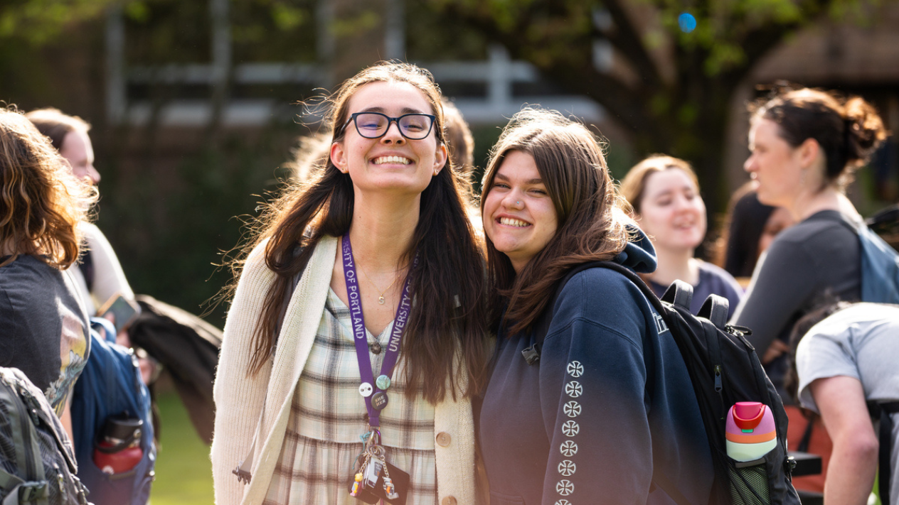 Two smiling students embrace on a sunny day in the quad