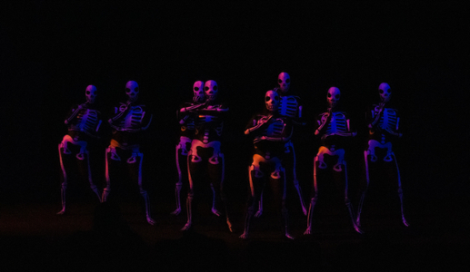 People in skeleton outfits dance in red and blue light