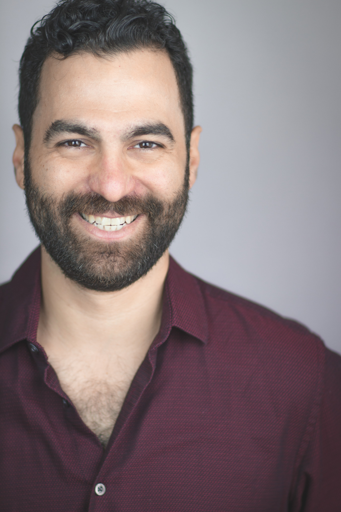 A man with brunette hair and a beard smiling to camera