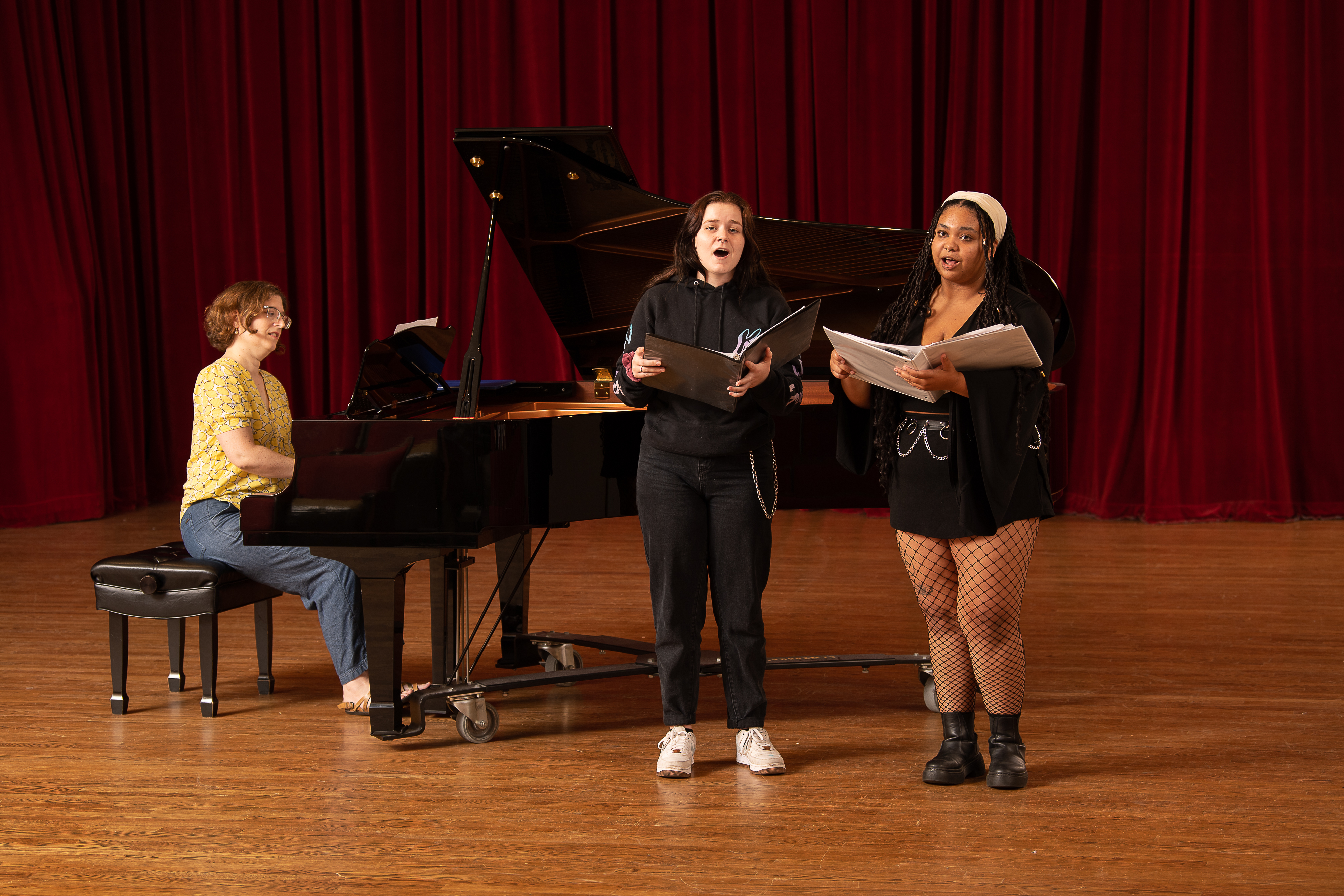 two students and a faculty pianist on stage performing a song